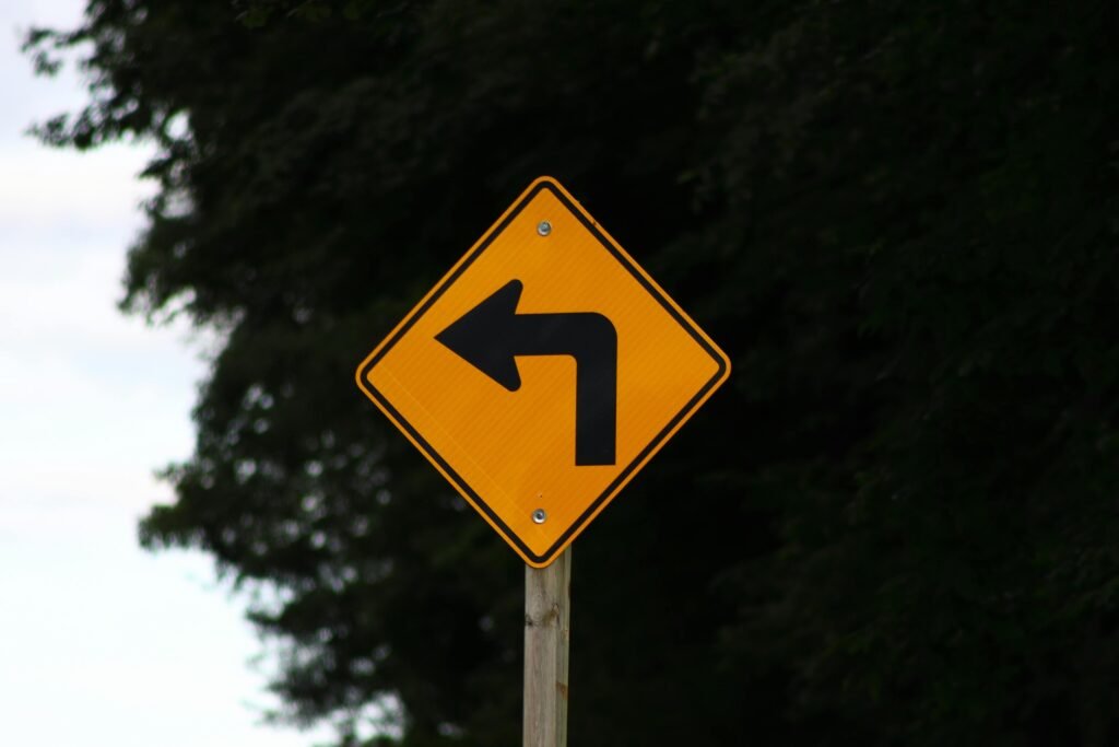 Regulatory compliance Close-up of a yellow left turn warning sign on a rural road.
